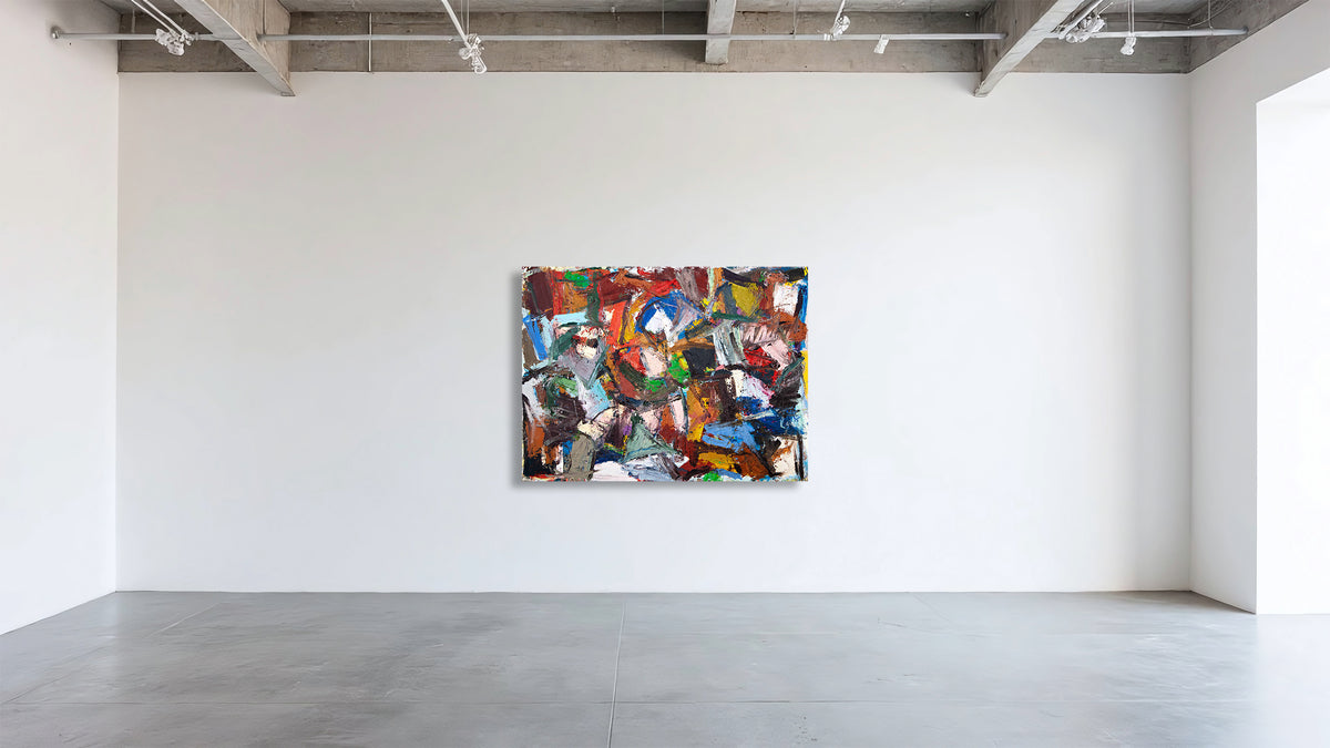 An abstract multicolor painting with bold brushstrokes in red, blue, green, yellow, and white, displayed on a white gallery wall in a modern studio space with concrete floors and ceiling.